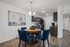 Modern dining area with elegant blue chairs and a round wooden table, adjacent to a sleek kitchen with stainless steel appliances and dark cabinets.