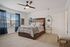 Elegant bedroom featuring a plush bed with stylish bedding, modern ceiling fan, and natural light flowing through large windows with blue curtains.