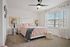 Bright and inviting bedroom with plush carpeting, chic ceiling fan, and elegant decor, featuring a large window for natural light.