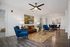 Elegant living room with modern decor featuring plush blue chairs, a stylish brown leather sofa, and ambient lighting. Vibrant artwork and wood flooring create a cozy, inviting atmosphere.