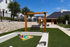Inviting outdoor area with lush green lawn, stone retaining wall, and cozy seating under wooden pergolas, perfect for relaxation and leisure activities.