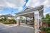 Charming residential entrance with stone pillars and a well-maintained driveway under a bright blue sky.