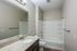 Elegant bathroom with a granite countertop, large mirror, and pristine white shower-tub combo, offering a tranquil atmosphere.