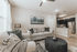 Inviting living room with stylish gray sofa and decorative pillows, featuring an open kitchen with modern appliances and elegant lighting.