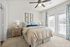 Bright and inviting bedroom with plush bedding, elegant curtains, and soft carpet, featuring modern ceiling fan and tasteful decor.