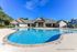 Inviting swimming pool area at a modern residential complex under a clear blue sky, with stylish poolside seating and lush greenery.