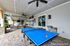 Luxurious outdoor entertainment space with ping pong table, cozy wicker seating, ceiling fans, and lush greenery, perfect for relaxation and fun.