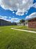 Expansive green lawn with modern buildings under a vibrant blue sky adorned with fluffy clouds.