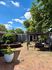 Charming outdoor patio with cozy seating, lush greenery, and a clear blue sky.