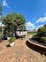 Charming courtyard with brick pathway, lush greenery, and stylish seating under a sunny blue sky.