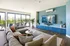Contemporary living room with a large gray sectional sofa, blue accent wall with TV, and floor-to-ceiling windows opening to a terrace.