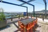Chic outdoor terrace with orange chairs and table, overlooking a stunning marina view beneath a blue pergola structure.