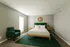 Elegant bedroom showcasing a plush bed with a green headboard, matching armchair, and stylish decor in a sunlit space.