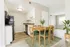 Bright and inviting open-concept dining area with stylish wooden furnishings, modern kitchen, and lush greenery, perfect for cozy gatherings.