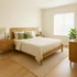 Bright and inviting bedroom with modern wooden furniture and elegant decor, featuring a cozy queen-sized bed and lush green plant.