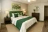 Inviting bedroom with a plush green and white bed, modern decor, ambient lighting, and elegant wooden flooring.