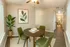 Chic dining area with a round table, green cushioned chairs, elegant potted plant, and stylish leaf artwork, offering a warm and inviting atmosphere.