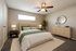Inviting bedroom with a cozy queen-sized bed, modern ceiling fan, elegant wooden dresser, and soft natural lighting, accented by lush greenery for a serene ambience.