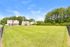 Charming suburban setting with lush green lawn, bordered by picturesque homes and vibrant trees under a clear blue sky.