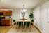 Elegant dining area with a modern wooden table, green velvet chairs, and stylish decor, adjacent to a cozy kitchen with warm wooden cabinets.
