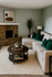 Cozy living room with a stylish beige sectional, brick fireplace, and elegant decor. Modern art and lush green accents create a warm, inviting space.