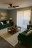 Inviting living room with elegant green sofas, a chic wooden coffee table, and abundant natural light through vertical blinds.