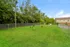 Vibrant green outdoor space featuring a fenced-in dog park with lush trees and a cozy seating area next to an inviting residential building.