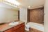 Elegant bathroom featuring a chic granite countertop, warm wood cabinetry, and sleek tiled shower in a modern apartment.