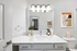Bathroom with quartz counters, large mirror, vanity lighting, and white cabinetry