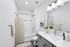 Bathroom with quartz counters, large mirror, vanity lighting, and white cabinetry