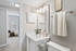 Bathroom with white counters, large mirror, vanity lighting, and white cabinetry.