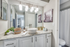 Bathroom with granite counters, large mirror, vanity lighting, and white cabinetry.