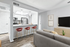 Vinyl floor living space with grey couch, wall art, ceiling fan, kitchen bar, and bar chairs