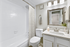 Bathroom with white counters, large mirror, vanity lighting, white cabinetry, shower, and toilet