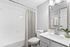 "Bathroom with white counters, large mirror, vanity lighting, white cabinetry, shower, and toilet