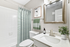 "Bathroom with white counters, large mirror, vanity lighting, white cabinetry, shower, and toilet