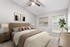 Carpeted bedroom with ceiling fan, beige bedding, large window, and wall art.