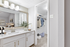 Bathroom with white counters, large mirror, vanity lighting, and white cabinetry.