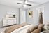 Carpeted bedroom with ceiling fan, beige bedding, dresser and wall art