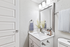 Bathroom with white counters, large mirror, vanity lighting, and white cabinetry