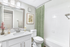 Bathroom with white counters, large mirror, vanity lighting, white cabinetry, shower, and toilet