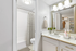 Bathroom with white counters, large mirror, vanity lighting, white cabinetry, shower, and toilet