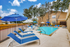 Pool with blue lounge chairs, sundeck, umbrellas, and trees