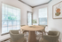 Dining area with three windows, wooden circular table, and four chairs.
