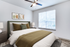 Carpeted bedroom with bed, ceiling fan, large window, and wall art