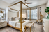 Carpeted bedroom with bed, ceiling fan, large window, ottoman, side tale and lamp