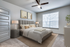 Carpeted bedroom with bed, ceiling fan, large window, side table, and lamp.