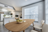 Dining area with three windows, wooden table, and four chairs.