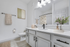 Bathroom with quartz counters, large mirror, vanity lighting, and white cabinetry
