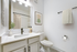 Bathroom with white counters, large mirror, vanity lighting, and white cabinetry